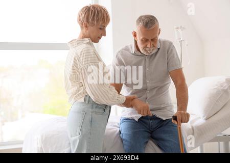 Reife Frau hilft ihrem Mann mit Stock in der Klinik Stockfoto