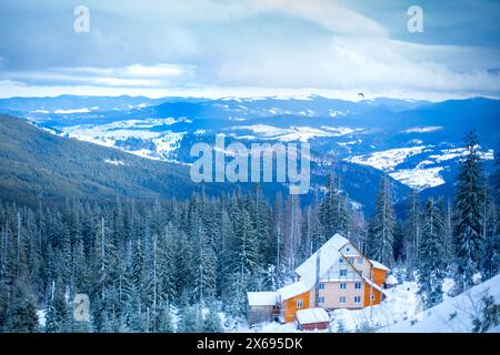 Schneebedeckte Skigebiete, hohe Kiefern, Hotel oder Haus aus Holz und Backstein, sanft verwischter blauer Berggrund Stockfoto
