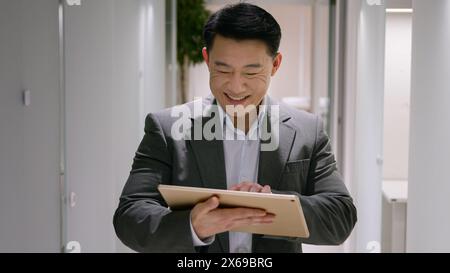Glücklicher asiatischer ethnischer Mann mittleren Alters chinesischer koreanischer Geschäftsmann lächelnder Geschäftsgeber Verwenden Sie ein digitales Tablet im Büro Flur Lobby männlicher Unternehmer Stockfoto