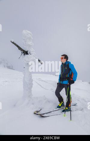 italien, Trentino, Primiero San Martino di Castrozza, Skibergsteiger in der Nähe eines vollständig mit gefrorenem Schnee bedeckten Kreuzes in der Nähe des Gipfels Juribrutto, Dolomiten Stockfoto