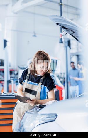 Der penible Service des Servicetechnikers im Auto verwendet ein Tablet, um die Rechnung für den Kunden nach der Reparatur des Kraftstofftanks zu berechnen. Fokussierter Werkstattspezialist berechnet die Endkosten nach der Wartung des Kundenfahrzeugs Stockfoto