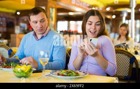 Modernes Paar, das während des Mittagessens im Restaurant Mobiltelefone benutzt Stockfoto