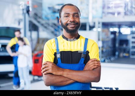 Porträt eines lächelnden BIPOC-Mechanikers in der Autowerkstatt, der mit dem Wechseln der Bremsflüssigkeit beauftragt ist. Zertifizierter Mitarbeiter in der Garage, der bereit ist, mit der Überprüfung von Fahrzeugen in der Garage zu beginnen Stockfoto