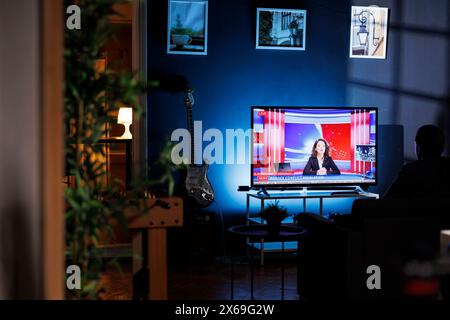 Entspannte Person, die nachts Nachrichten im Fernsehen sah, auf dem Sofa im Wohnzimmer chillt und fernsehsendungen ansah. Junge Erwachsene, die Medieninformationen über ein globales Netzwerk hören. Stockfoto
