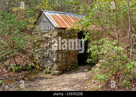 Ein Bach, der durch das alte Steinquellhaus mit Metalldach fließt, eingebettet in den Wäldern in den Bergen, wo es früher Gehöfte gab Stockfoto