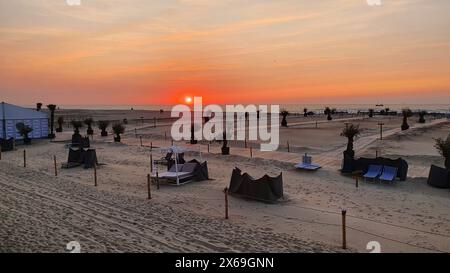 Breiter Sandstrand am Meer mit vielen Liegen, Palmen, Cafe und Hotel. Sonnenuntergang am Strand. Stockfoto