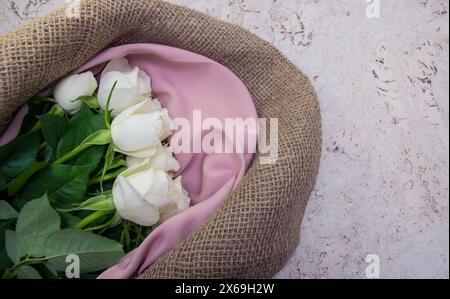 Weißer Rosenstrauß in Naturstoff-Wickelpapier. Frühlingsblumen auf dem Korkhintergrund . Draufsicht mit Platz für Text. Kopierbereich. Stockfoto