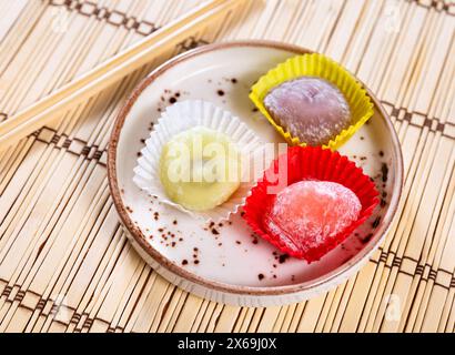 Bunte Mochi-Desserts in Papiereinlagen auf Teller über Bambusmatte Stockfoto