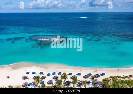 Aus der Vogelperspektive auf das türkisfarbene Wasser am Shoal Bay Beach mit Sonnenschirmen und Palmen in Anguilla. Stockfoto