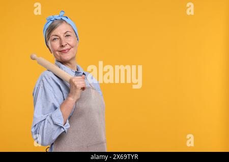 Glückliche Hausfrau mit rollendem Pin auf orangem Hintergrund, Platz für Text Stockfoto