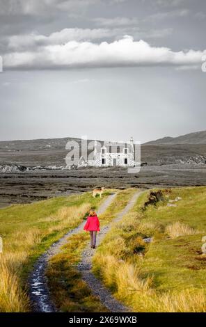 Verlassene, ruinierte Crofters beherbergen croft in Minish. West End von Loch Maddy. Nord-Uist, Äußere Hebriden, Schottland. Frau und Hund gehen auf dem Weg Stockfoto