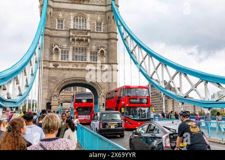 Tower Bridge London, Fußgänger gehen über die Brücke neben London Black Taxi, männlichen Radfahrern und zwei Londoner Doppeldeckerbussen, England, 2023 Stockfoto