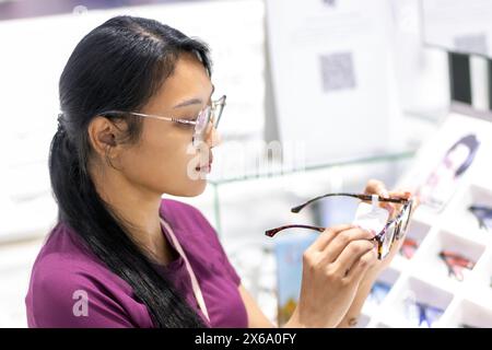 Eine junge Frau wählt Brillen in einem Optikgeschäft Stockfoto