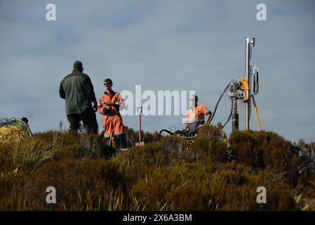 HAUPIRI, NEUSEELAND, 7. MAI 2024: Bohrer betreiben ein tragbares Bohrgerät, um ein 10 Meter langes Loch auf dem Gipfel des Mount Morgan mit Blick auf das Haupiri Valley an der Westküste Neuseelands zu versenken. Das Loch wird für seismische GPS-Überwachungsinstrumente verwendet, um die Bewegung entlang der Alpenverwerfung zu messen, die sich in der Nähe des Berges befindet. Die gesamte Bohrausrüstung einschließlich Luftkompressor, Generator und Bohrgerät wurde per Hubschrauber zum Gipfel geflogen. Stockfoto