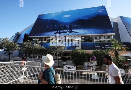 Cannes, Frankreich. Mai 2024. Die Menschen gehen an einem riesigen Poster der 77. Ausgabe der Filmfestspiele von Cannes vor dem Palais du Festival in Cannes, Südfrankreich, vorbei, 13. Mai 2024. Das diesjährige Festival findet vom 14. Bis 25. Mai statt. Quelle: Gao Jing/Xinhua/Alamy Live News Stockfoto