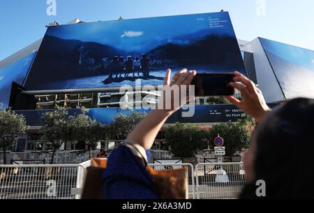 Cannes, Frankreich. Mai 2024. Eine Frau fotografiert ein riesiges Poster der 77. Ausgabe der Filmfestspiele von Cannes vor dem Palais du Festival in Cannes, Südfrankreich, 13. Mai 2024. Das diesjährige Festival findet vom 14. Bis 25. Mai statt. Quelle: Gao Jing/Xinhua/Alamy Live News Stockfoto