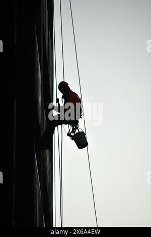 Silhouette eines Mannes, der sich abseilt und Fenster in einem Hochhaus wäscht Stockfoto