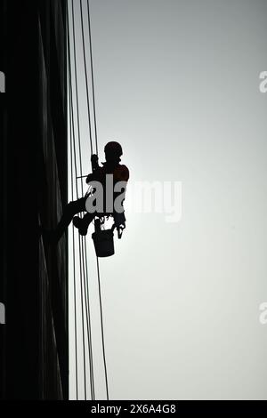 Silhouette eines Mannes, der sich abseilt und Fenster in einem Hochhaus wäscht Stockfoto