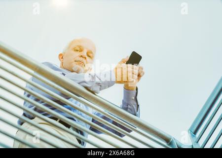 Im Außenbereich wird ein Mann intensiv mit seinem Smartphone erfasst, unterstützt durch ein Metallgeländer bei Sonnenlicht Stockfoto