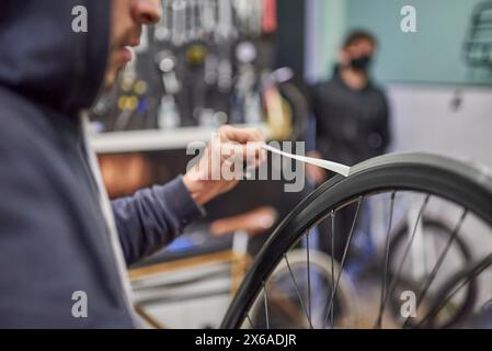 Mann, der an einem Fahrradgemälde arbeitet. Zeit zum Entfernen des Abdeckbands der Radfelge. Nahansicht. Stockfoto