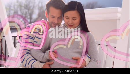 Bild von Herzsymbolen über glücklichem kaukasier, der schwangere Frau umschließt Stockfoto