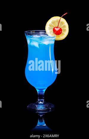 Blue Lagoon Cocktail garniert mit Zitronenscheibe und Kirsche serviert in einem klassischen Hurrikanglas isoliert auf schwarzer reflektierender Oberfläche und dunklem Hintergrund Stockfoto