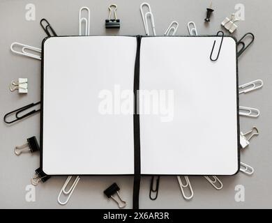 Nahaufnahme eines Notizblocks mit leeren Seiten und verschiedenen Arten von Büroklammern auf grauem Hintergrund Stockfoto