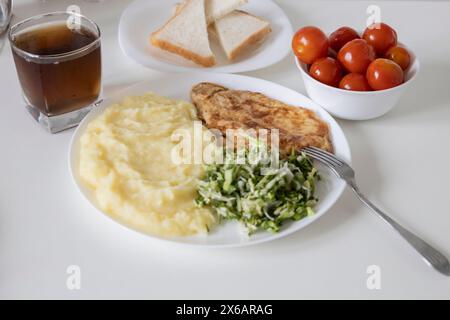 Tee in einem Glas und eingelegte Tomaten auf einem weißen Teller und Scheiben Weißbrot. Leckeres Frühstück oder Mittagessen mit Kartoffelpüree, Hähnchenkotelett mit Salat - Stockfoto