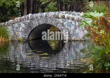 Eine Steinbogen-Fußgängerbrücke in den Queenstown Botanical Gardens, Neuseeland. Stockfoto