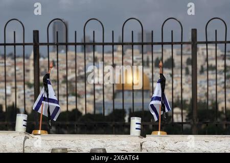 JERUSALEM - 12. MAI: Israelische Nationalflaggen mit schwarzen Trauerbändern sitzen auf dem jüdischen Friedhof im Ölberg über den Gräbern der gefallenen israelischen Soldaten, im Hintergrund der islamische Schrein Kuppel des Felsens. während sich das Land auf den Gedenktag des Yom Hazikaron für die gefallenen Soldaten am 12. Mai 2024 in Jerusalem vorbereitet. Israel Stockfoto