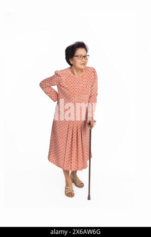 Alte Frau mit Schmerzen im unteren Rücken auf weißem Hintergrund, stehend mit Gehstock Stockfoto