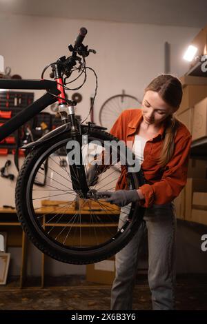 Blonde Frau repariert ihr Fahrrad. Die Dame repariert ihr Fahrrad, während sie in der Garage arbeitet. Fahrradmechaniker. Stockfoto