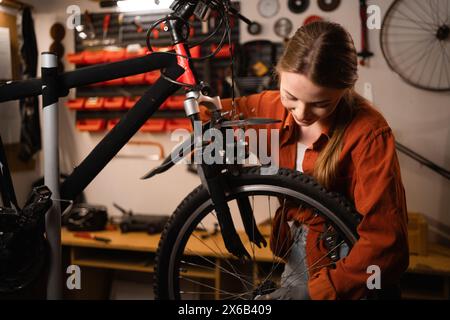 Porträt einer kaukasischen Mechanikerin in der Nähe eines Fahrrades in der Werkstatt. Frau Meister, Spezialist für Fahrradreparatur, in atmosphärischer Garage Stockfoto