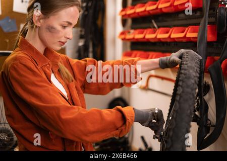 Eine Mechanikerin, die ein Fahrrad in einer Werkstatt oder Garage repariert, überprüft ein Rad auf Installation. Stockfoto