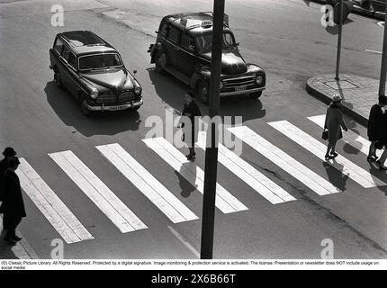 Fahren in den 1950er Jahren Die Leute kommen auf einer Zebraüberquerung vorbei und zwei Volvo-Autos halten an, um sie passieren zu lassen. Schweden 1960 Stockfoto