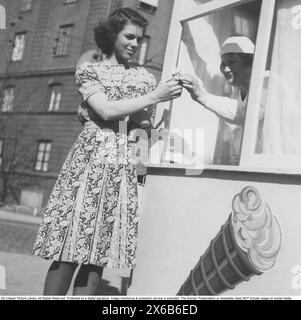 Eis in den 1940er Jahren Die Frau, die Eis verkauft, übergibt dem Kunden durch das Fenster ihres Kiosks den Kegel Vanilleeis. 1944 Stockfoto