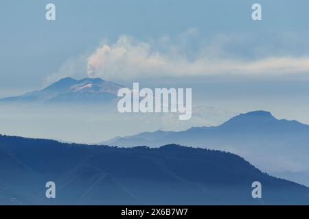 Rauch steigt aus dem aktiven Ätna-Vulkan auf Sizilien an einem trüben blauen Tag aus PALMI, Kalabrien, Italien Stockfoto