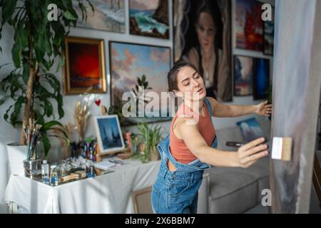 Die Künstlerin führt selbstbewusst einen breiten Pinsel und wischt die Leinwand von Schmutzstaub ab. Maler in der Kunstwerkstatt. Stockfoto