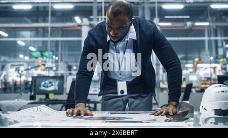 Afroamerikanischer Ingenieur, der einen technischen Blueprint bei der Arbeit in einem Büro in einem Automontagewerk ansieht. Industriespezialist, der an Fahrzeugteilen in der technischen Entwicklungsanlage arbeitet. Stockfoto