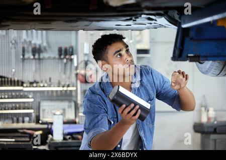 Mann, Mechaniker und Unterseite des Fahrzeugs in der Werkstatt für Arbeiten oder Wartung, Inspektion und Ölwechsel mit Licht. Person, Motor und Garage für Motor oder Stockfoto