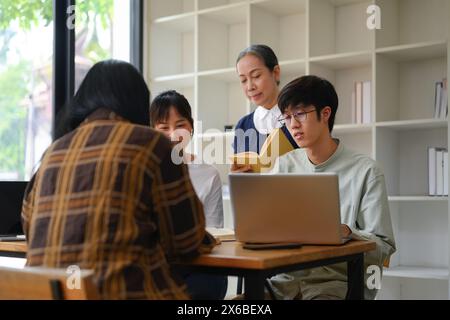 Glücklicher, reifer Professor, der einer Gruppe von Studenten in der Universitätsbibliothek hilft Stockfoto