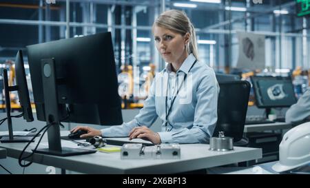 Autowerkstatt: Porträt einer selbstbewussten Chefingenieurin, die am Desktop-Computer arbeitet. Professioneller Techniker in der Herstellung von automatisierten Roboterarmen in der Fertigung von High-Tech-Elektrofahrzeugen Stockfoto