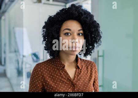 Selbstbewusste Geschäftsfrau posiert in einem modernen Büroumfeld mit Glaswänden und moderner Einrichtung, die Professionalität und Erfolg zum Ausdruck bringt. Stockfoto