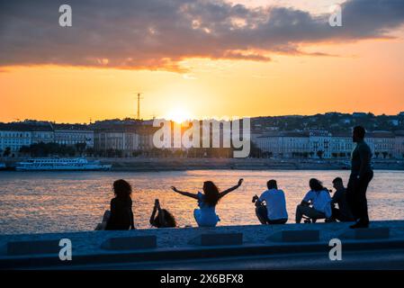 Gruppe von Menschen, die den Sonnenuntergang am Fluss in der Stadt beobachten Stockfoto