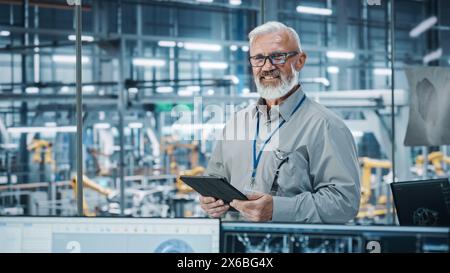 Autowerkstatt: Porträt eines leitenden weißen männlichen Chefingenieurs mit Tablet-Computer in automatisierten Roboterarmmontagestraßen zur Herstellung von High-Tech-Elektrofahrzeugen. Die Kamera anschauen und lächeln Stockfoto