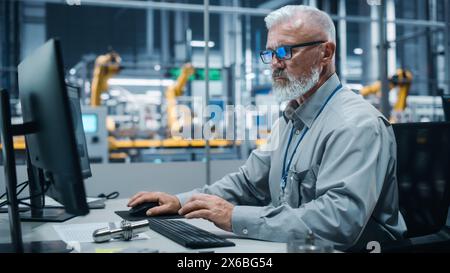 Autowerkstatt: Porträt eines männlichen Ingenieurs, der am Computer arbeitet. Automatisierte Roboterarm-Montage-Fertigungslinie Für Elektrofahrzeuge. Techniker, Der Die Elektronikproduktionsförderer Überwacht. Stockfoto