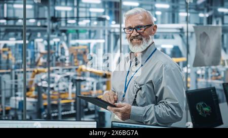 Autowerkstatt: Porträt eines leitenden weißen männlichen Chefingenieurs mit Tablet-Computer in automatisierten Roboterarmmontagestraßen zur Herstellung von High-Tech-Elektrofahrzeugen. Die Kamera anschauen und lächeln Stockfoto