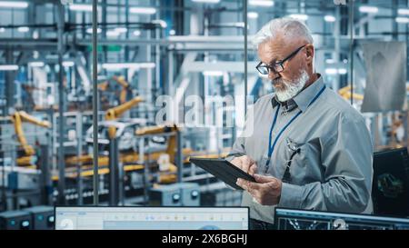 Autowerkstatt: Porträt eines leitenden weißen männlichen Chefingenieurs mit Tablet-Computer in automatisierten Roboterarmmontagestraßen zur Herstellung von High-Tech-Elektrofahrzeugen. Mittlere Aufnahme Stockfoto