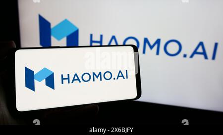 Person, die ein Smartphone mit dem Logo des chinesischen Autonome Fahrers Haomo hält. AI vor dem Monitor. Konzentrieren Sie sich auf die Mitte des Telefondisplays. Stockfoto