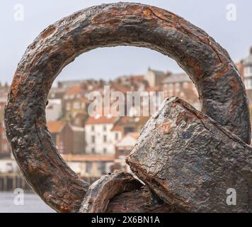 Eine Nahaufnahme eines alten rostenden und zersetzenden Ankerrings. Die Gebäude einer Hafenstadt sind in der Ferne zu sehen. Stockfoto